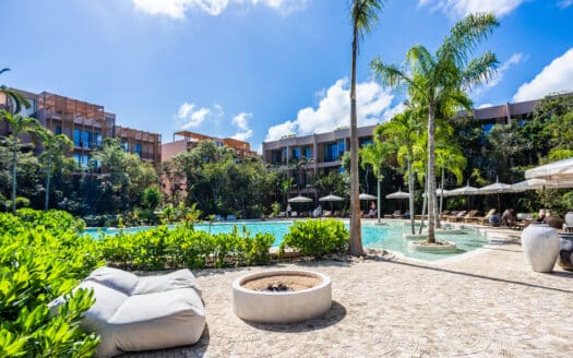Luxury pool area with sun loungers, lush greenery, and modern residential buildings in the background in Tulum at Aflora.