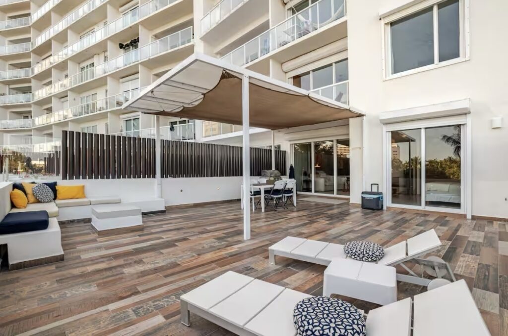 Outdoor terrace with lounge chairs, seating area, and retractable awnings overlooking a high-rise building at beachfront property in Cancun at Amara Beachfront Condo.