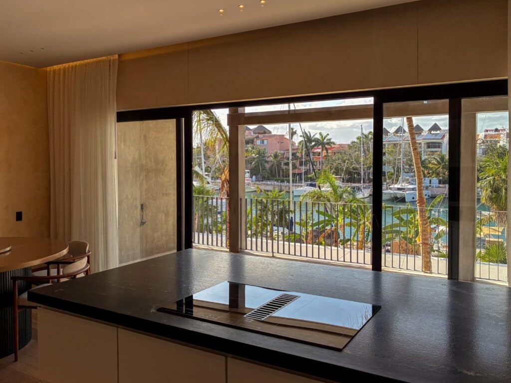 Interior view of a condo with large sliding glass doors overlooking a marina with boats and palm trees at Artesan Condo in Caleta Xel - Ha, Puerto Aventuras.