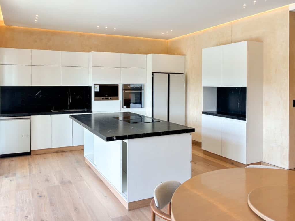 Modern kitchen with white cabinetry, black countertops, built-in appliances, and a wooden floor in Artesan Penthouse at Caleta Xel - Ha, Puerto Aventuras.
