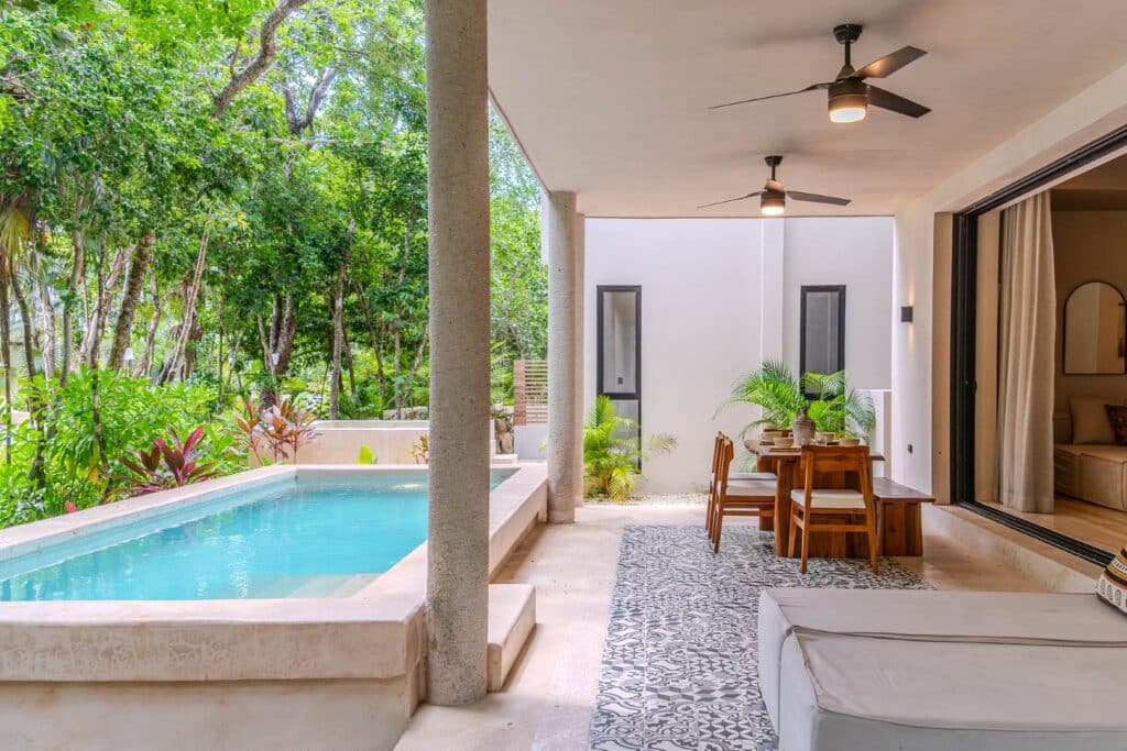 Open-air living area with pool, surrounded by lush greenery in a property in Holistika, Tulum.