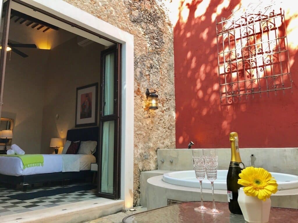 Interior view of a bedroom with an open door leading to an outdoor space featuring a hot tub, champagne, and yellow flower in Merida at Barrio De Santiago Villa.