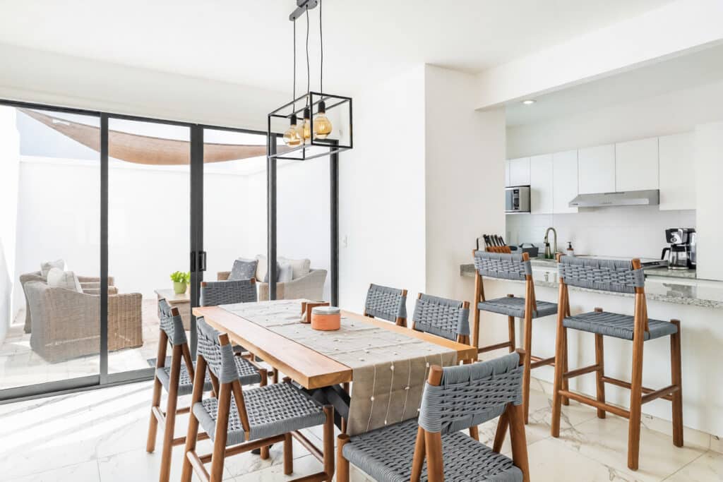 Modern dining area with a wooden table, eight chairs, and a view of an outdoor patio at Capri 9 – House in Playa del Carmen.