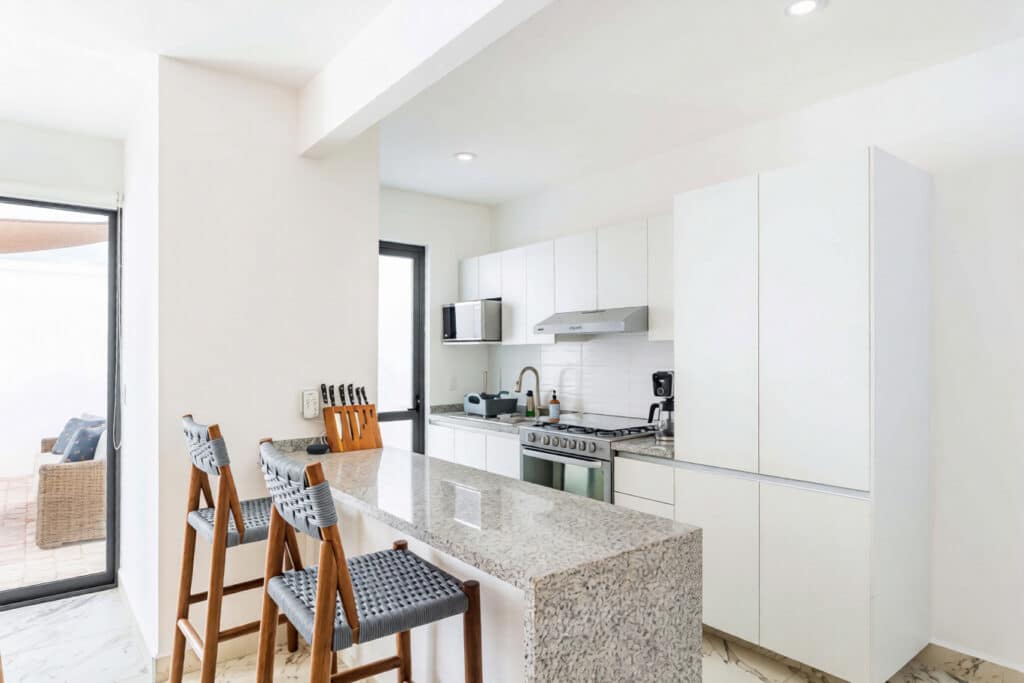 Modern white kitchen with granite counter and high chairs at property at Capri 9 – House in Playa del Carmen.