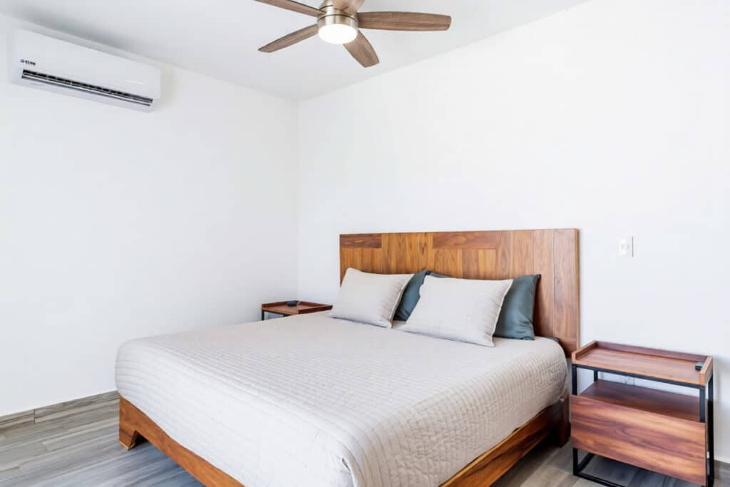 Modern bedroom with wooden headboard, ceiling fan, air conditioning, minimalist nightstands, and neutral-colored bedding at Capri 9 – House in Playa del Carmen.