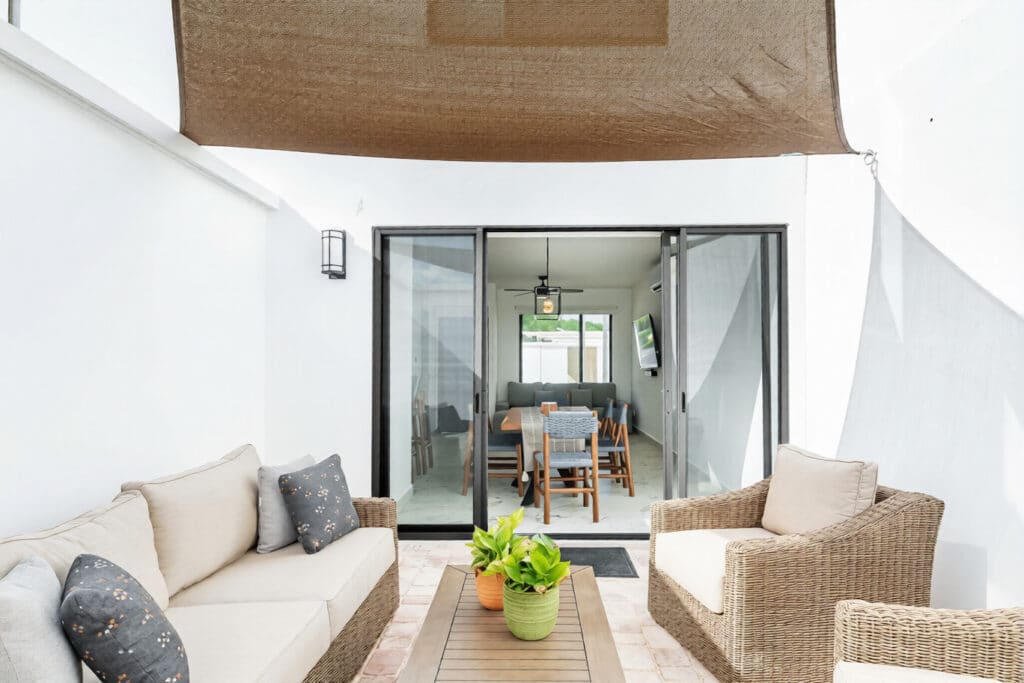 Patio with wicker furniture, potted plants, and a view of an interior dining area with sliding glass doors at Capri 9 – House in Playa del Carmen.