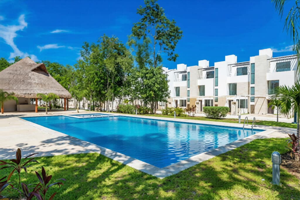 View of a swimming pool surrounded by lush greenery and modern white buildings at Capri 9 – House in Playa del Carmen.