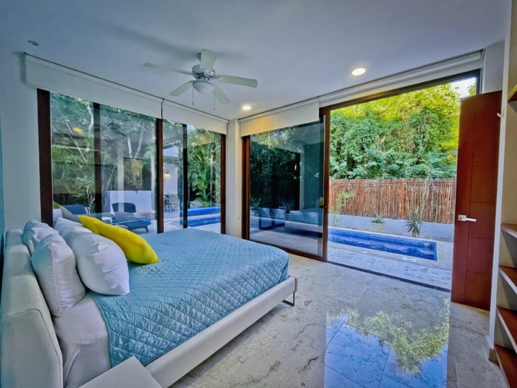 Bedroom with large glass sliding doors opening to a pool and jungle garden outside in Tulum. at Casa Bahamas in Tulum Country Club.