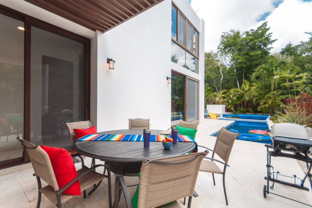 Outdoor patio with dining table, surrounded by lush greenery and a small pool at Casa Bahamas in Tulum Country Club.