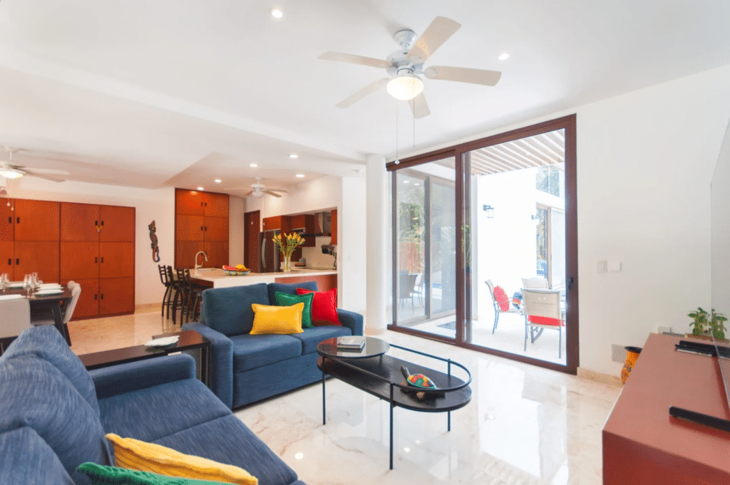 Living room with sliding glass doors opening to outdoor seating area, modern furniture, and a ceiling fan at Casa Bahamas in Tulum Country Club.