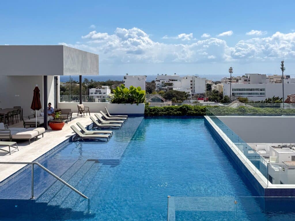 View of an outdoor swimming pool with lounge chairs and cityscape in Playa Centro, Playa del Carmen, seen from Ceiba at 25 2-Bedroom Condo.