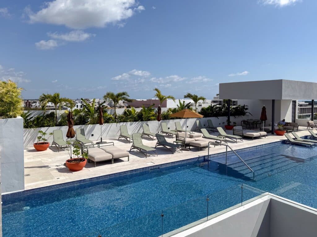 View of rooftop pool with lounge chairs, umbrellas, and tropical plants in a modern condo complex at Playa Centro, Playa del Carmen at Ceiba at 25 2-Bedroom Condo.