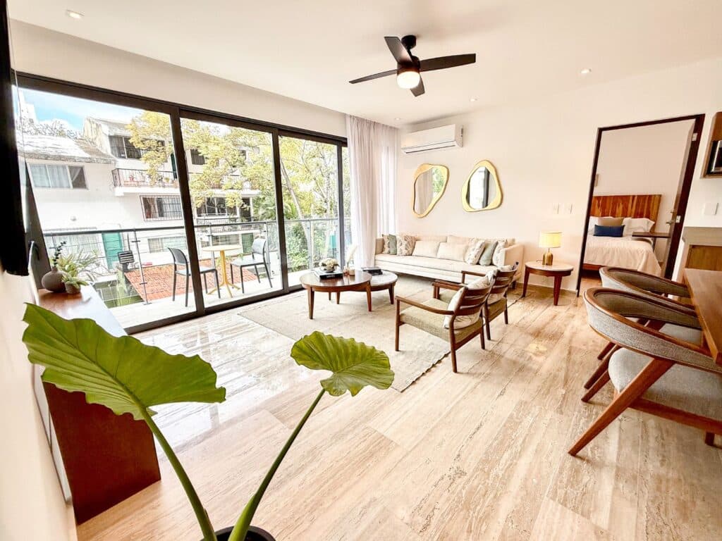 Living room with white sofa, wooden coffee table, armchairs, sliding glass doors opening to balcony, and modern decor in Playa Centro at Ceiba at 25 2-Bedroom Condo.
