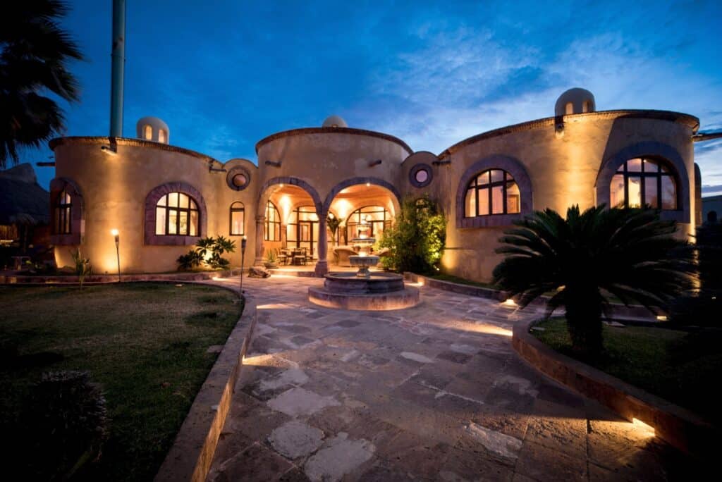 Exterior view of Casa de las Cúpulas Ocean View Villa with warm lighting, arched windows, and a fountain in the courtyard at Isla Punta Sur, Isla Mujeres.