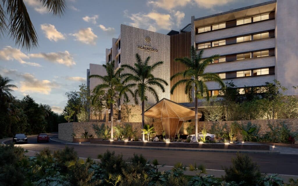 Distrito Xcalacoco 302 in Playa del Carmen features a modern building with a textured facade, palm trees, and outdoor lighting at dusk.