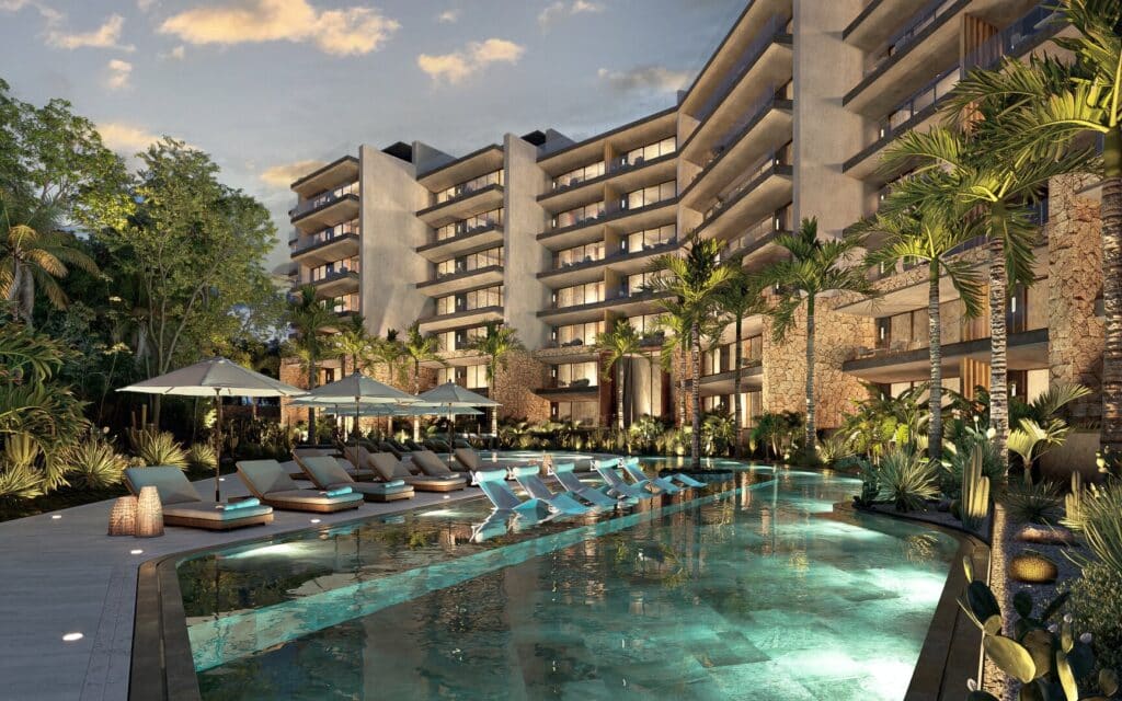 Modern Playa del Carmen condominium complex with an outdoor pool, sun loungers, umbrellas, and lush green landscaping.