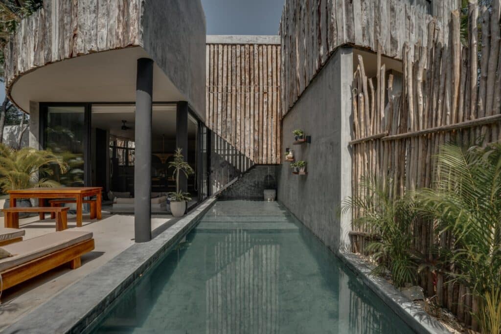 Modern villa with a narrow pool, glass sliding doors, and natural wood and concrete exterior at Esencia Villa in La Veleta, Tulum.