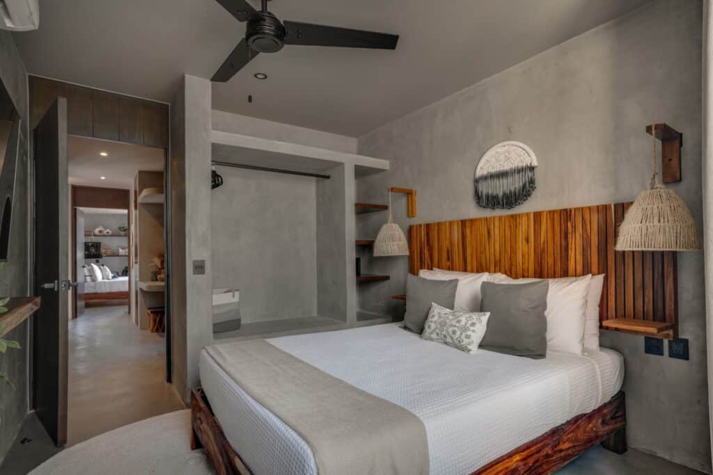 Modern bedroom with wooden headboard, gray walls, hanging wicker lamps, and an open closet at Esencia Villa in La Veleta, Tulum.