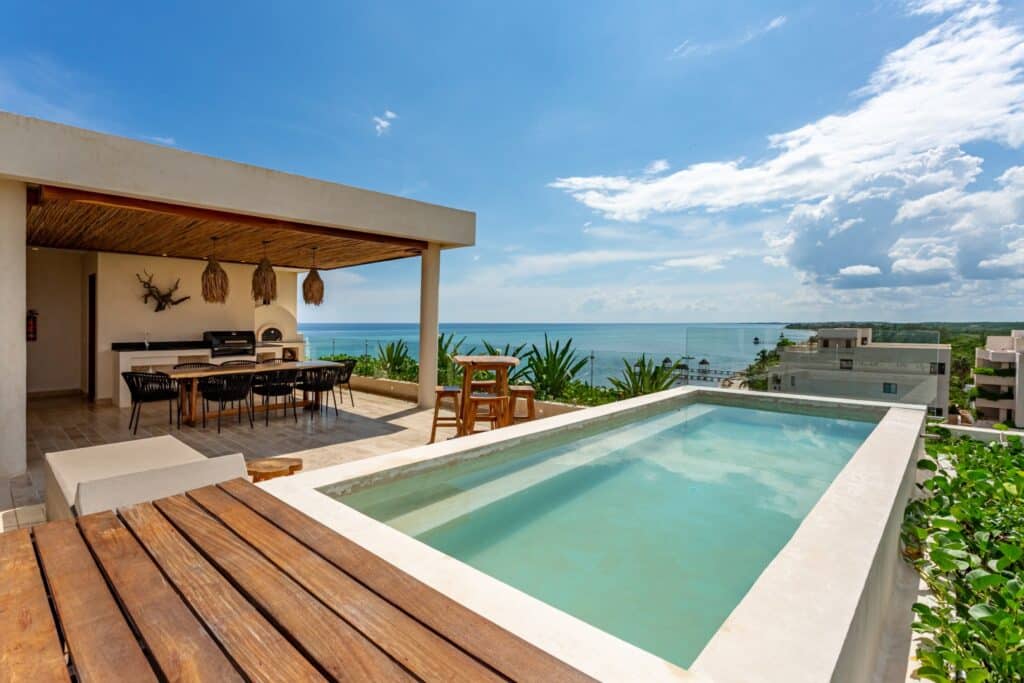 A rooftop terrace with a small pool, outdoor dining area, and panoramic ocean views in a beachfront property in Tulum at Kaoba Beachfront Condo.