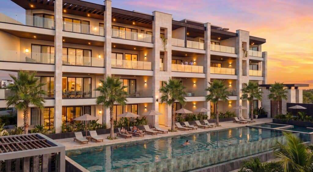 Luxury apartment with glass balconies overlooking a pool and palm trees at sunset at Luna Azul 103 in Bahia Xcacel, Puerto Aventuras.