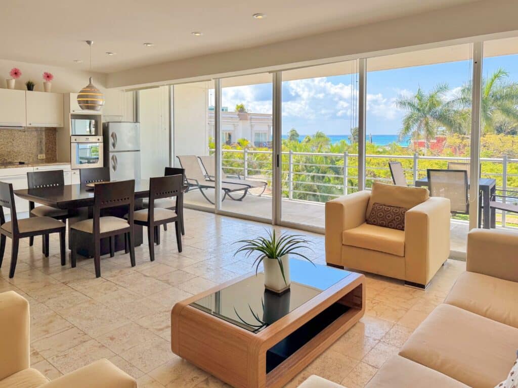 Bright living area with large sliding glass doors leading to a balcony view of trees, rooftops, and the ocean in Playa del Carmen. at Magia 202 F in Playa Centro, Playa del Carmen.