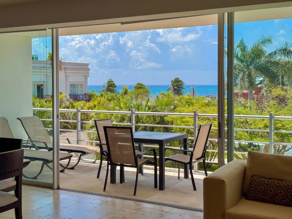 View from a condo balcony showing tropical trees, neighboring buildings, and the ocean in Playa Centro, Playa del Carmen. at Magia 202 F.