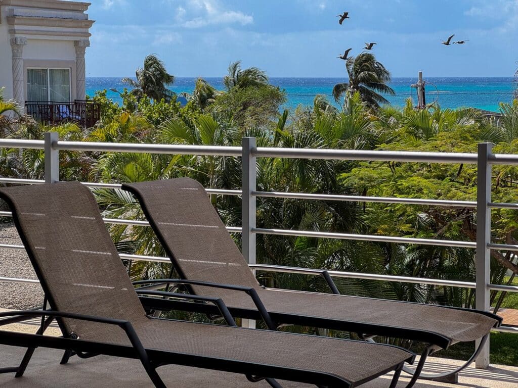 View of the ocean from a balcony with two lounge chairs, overlooking lush greenery and the Playa del Carmen coastline. at Magia 202 F in Playa Centro, Playa del Carmen.