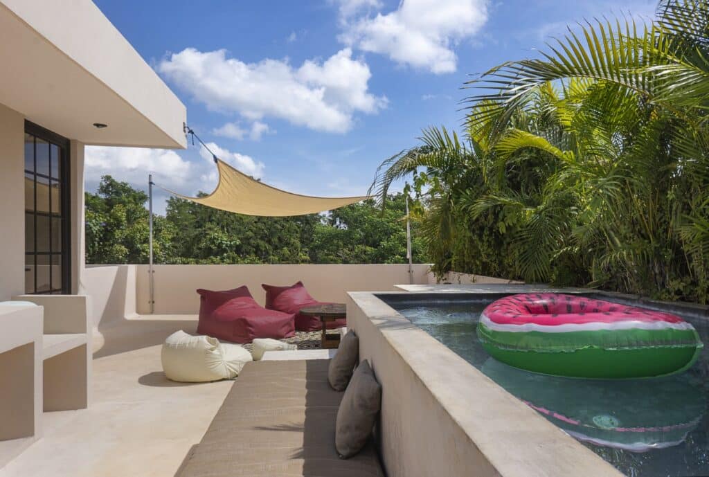 Outdoors at Maison Siscolino in Tulum's Region 15, featuring a small pool with a watermelon-themed float, shaded seating, and lush tropical plants.