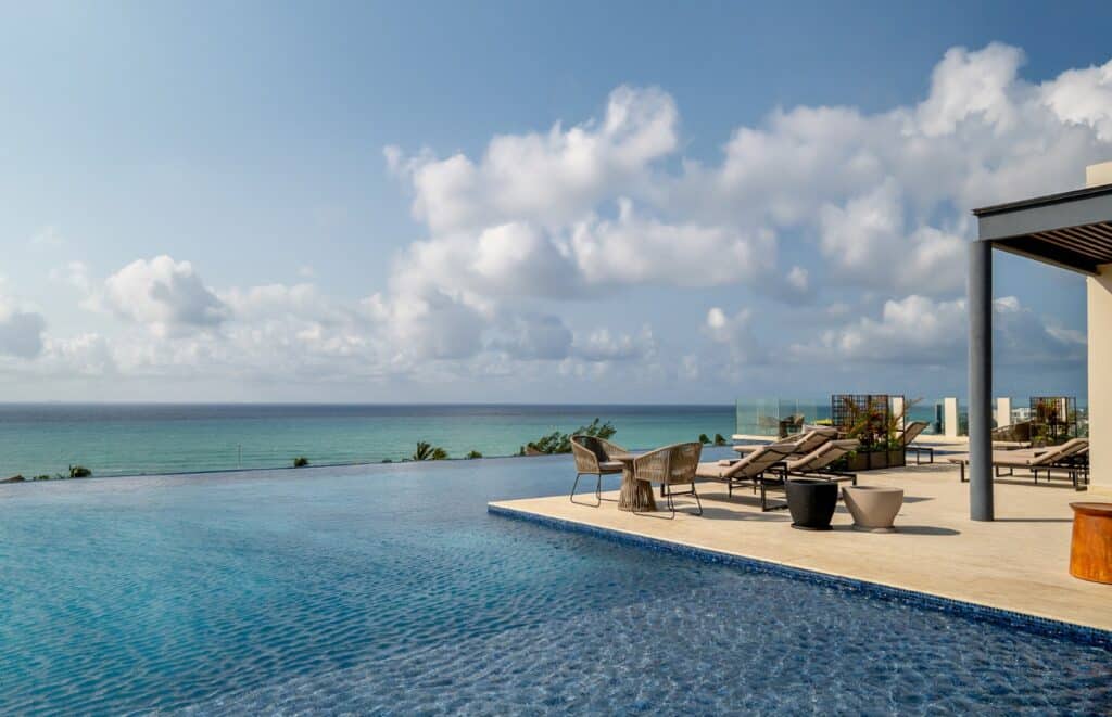 Poolside view with sun loungers, dining area, and ocean horizon at Marila Condo in Zazil Ha, Playa del Carmen.