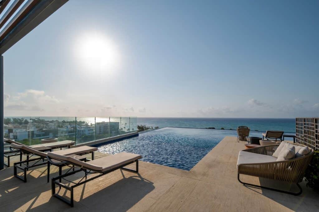 Rooftop infinity pool overlooking the ocean with lounge chairs and seating area at property at Marila Condo in Zazil Ha, Playa del Carmen.