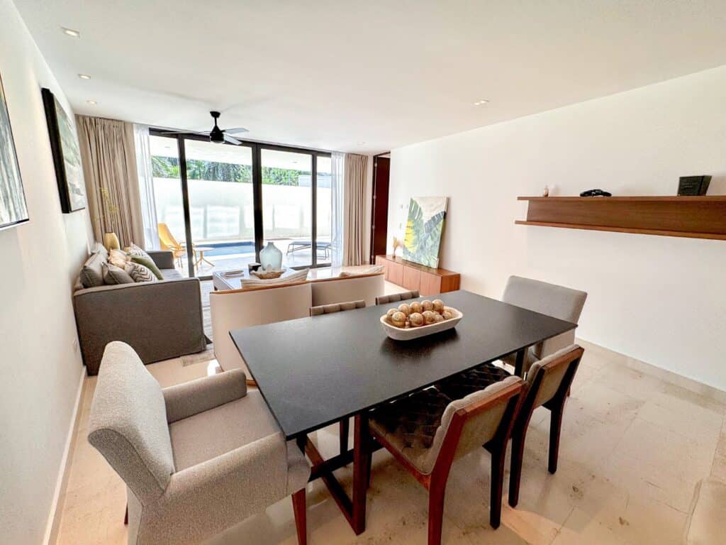 Open-concept living and dining room with large glass sliding doors leading to a balcony, bright decor, and minimalist furniture at Marila Condo in Zazil Ha, Playa del Carmen.