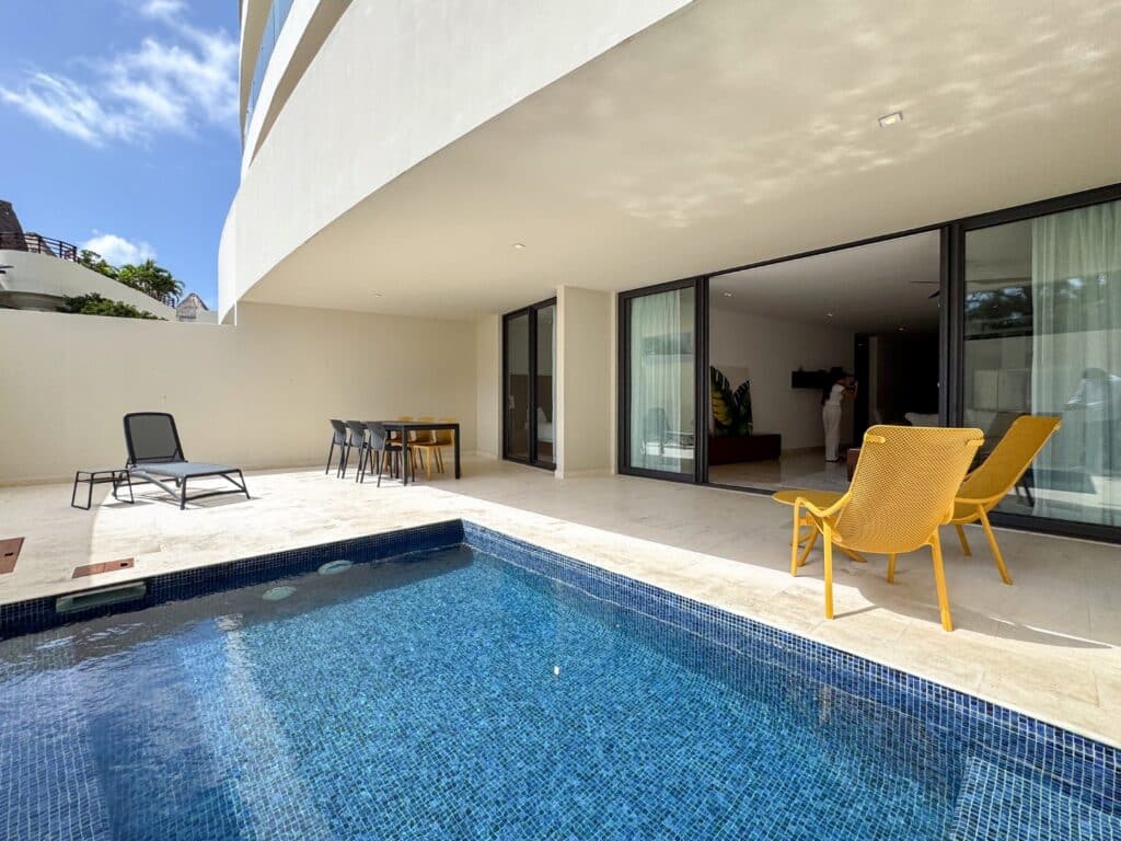View of a private pool area with yellow chairs and sliding glass doors in Marila Condo, Zazil Ha, Playa del Carmen.