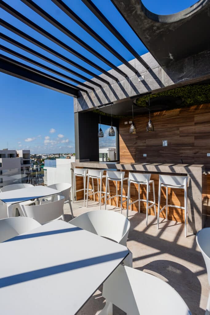 Rooftop terrace with white tables and chairs, wooden wall accents, pendant lamps, and a cityscape view in Playa del Carmen at My Menesse 407 Studio.