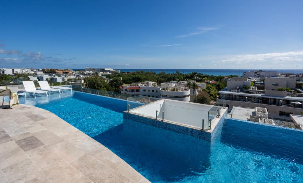 View of a rooftop infinity pool overlooking Playa del Carmen with white lounge chairs and cityscape in the background at My Menesse 407 Studio.