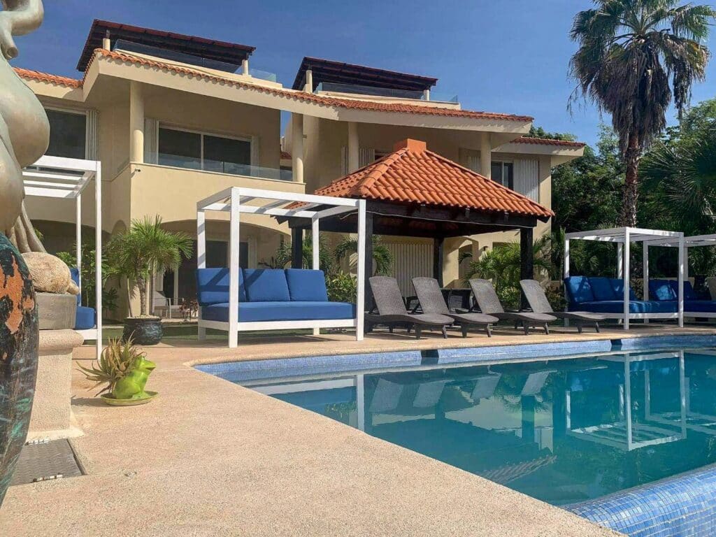 View of the swimming pool area with shaded cabanas and sun loungers at waterfront building at Nautica 8 Unit Marina Front Building in Boulevard Puerto Aventuras.