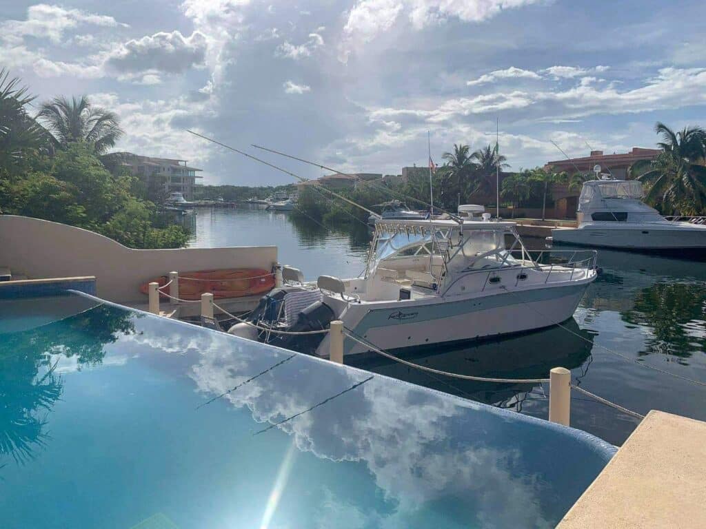 View of a yacht docked at a marina with palm trees and residential buildings, overlooking a calm waterway near Boulevard Puerto Aventuras at Nautica 8 Unit Marina Front Building.