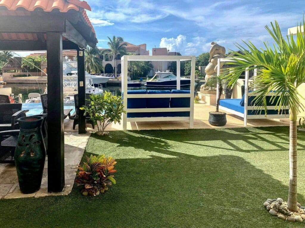 Exterior view of a marina-front property with outdoor seating, potted plants, and a waterway in the background at Boulevard Puerto Aventuras at Nautica 8 Unit Marina Front Building.