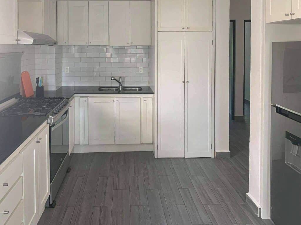 Kitchen with white cabinets, black countertops, gray flooring, and a stove, near a hallway in a property at Boulevard Puerto Aventuras at Nautica 8 Unit Marina Front Building.