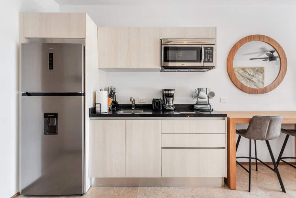 Modern kitchen with stainless steel refrigerator, microwave, coffee maker, and round mirror in a bright, minimalist space at Luis Donaldo Colosio, Playa del Carmen.