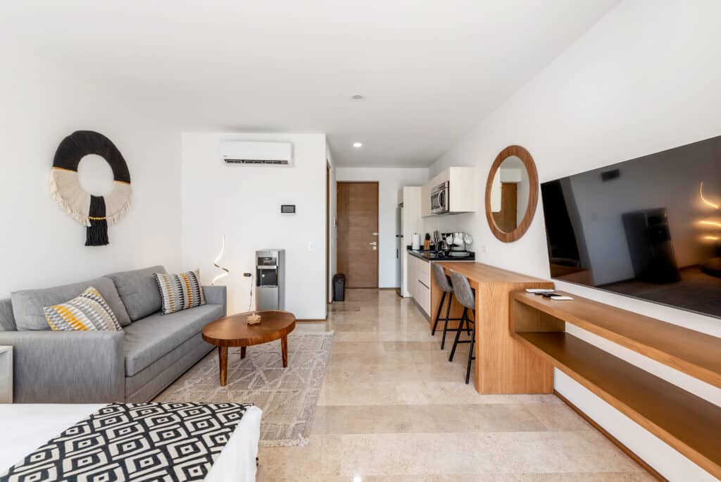 Interior view of a modern living area with a gray sofa, wooden coffee table, integrated kitchen, and flat-screen TV in a studio apartment in Playa del Carmen at Sea Tower Studio.