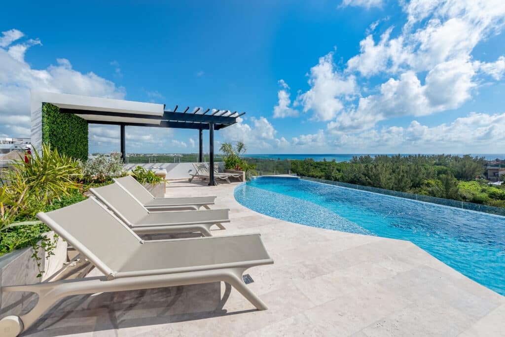 Poolside lounge chairs and lush green plants overlooking a distant ocean view with a bright blue sky at Sea Tower Studio in Luis Donaldo Colosio, Playa del Carmen.