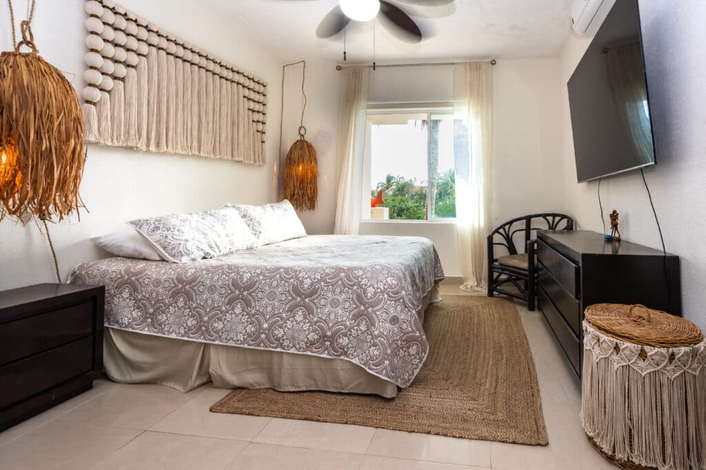 Bedroom with a patterned bedspread, large window with sheer curtains, and coastal decor in Puerto Aventuras at Sotavento Penthouse.