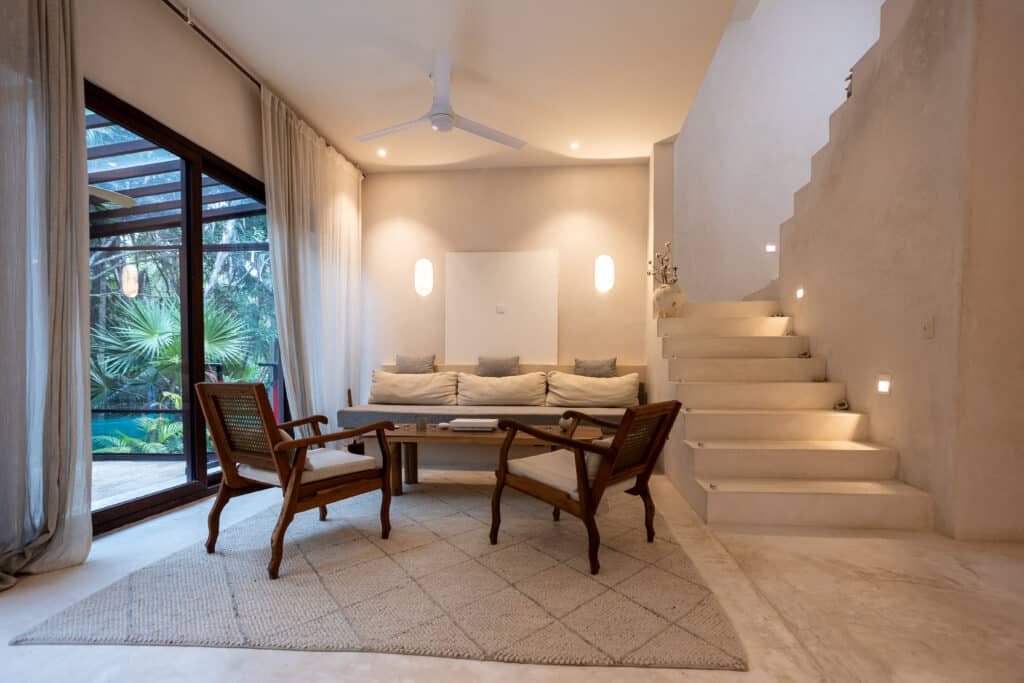 Living room with large glass sliding doors, beige curtains, a white ceiling fan, and staircase at Tao Ocean D1 at Tao Ocean D1 3-Bedroom House in Akumal.