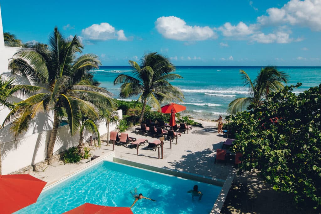 View of a beach with palm trees, lounge chairs, and a swimming pool overlooking the ocean at Tao Ocean H2 3-Bedroom House in Akumal.