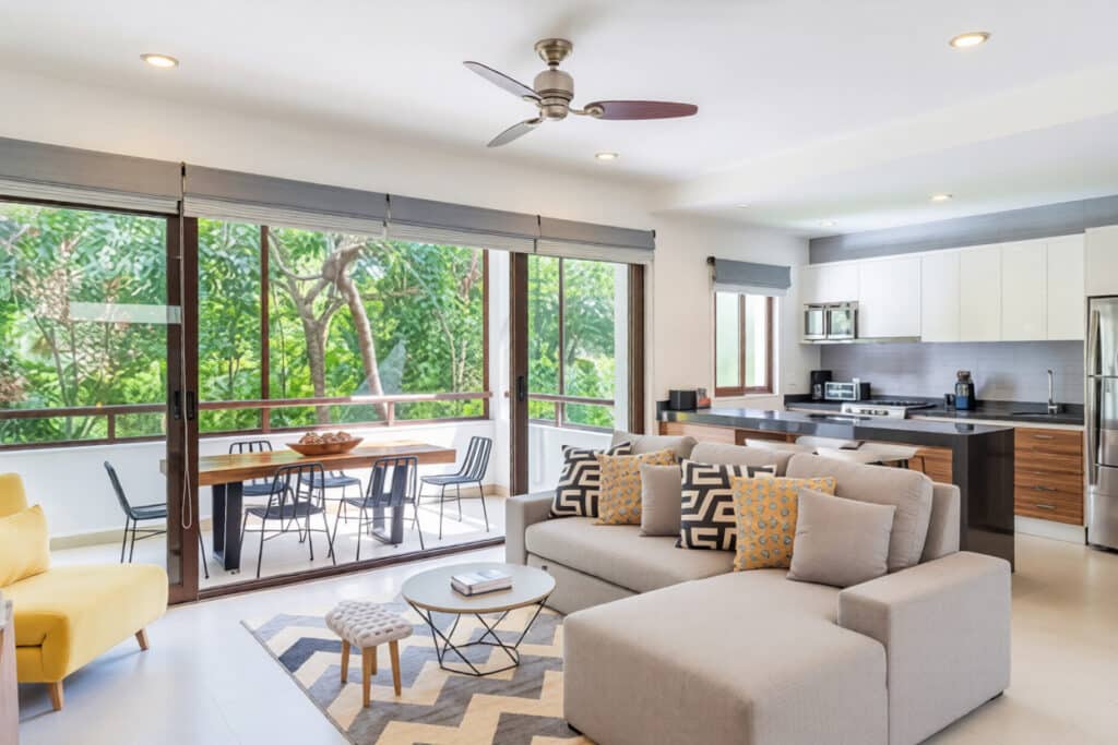 Modern kitchen and living area with large sliding glass doors opening to balcony overlooking lush greenery at Tao Tse M8 1-Bedroom Condo in Akumal.