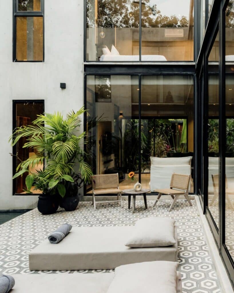 Modern outdoor living area with lounge seats, potted plants, and glass walls at Villa Asha in Aldea Zama, Tulum.