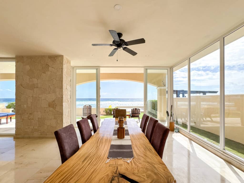 Interior view of Villa Coccoloba in Tulum featuring a dining area with a wooden table, large glass windows, and ocean views.