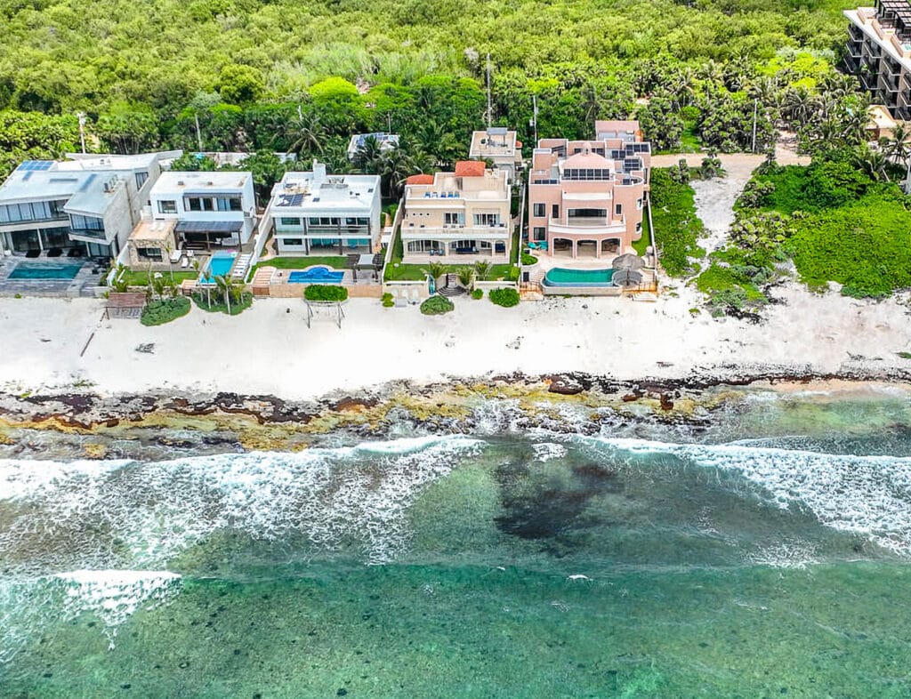 Aerial view of beachfront villas in Villa Coccoloba, Tulum, featuring modern architecture, private pools, and lush greenery on the coastline.