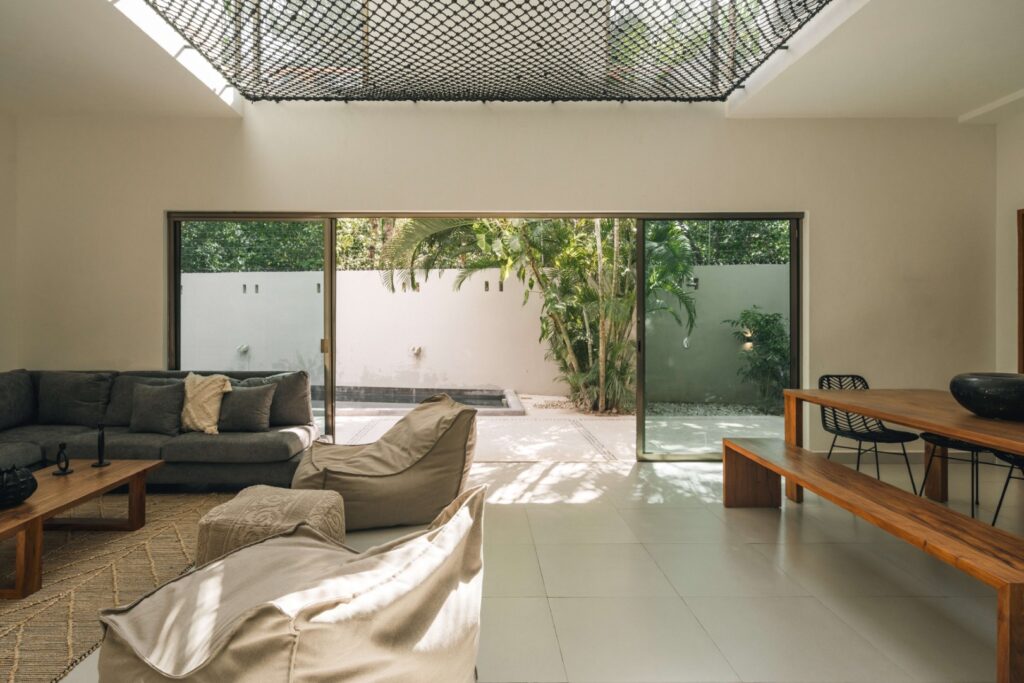 Living room with sliding glass doors opening to a lush outdoor space, contemporary furniture, and minimalist decor in Villa Esperia in Aldea Zama, Tulum.