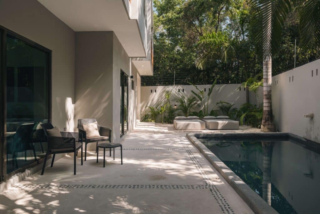 Patio area with seating, a small pool, lush tropical plants, and large glass sliding doors at Villa Esperia in Aldea Zama, Tulum.